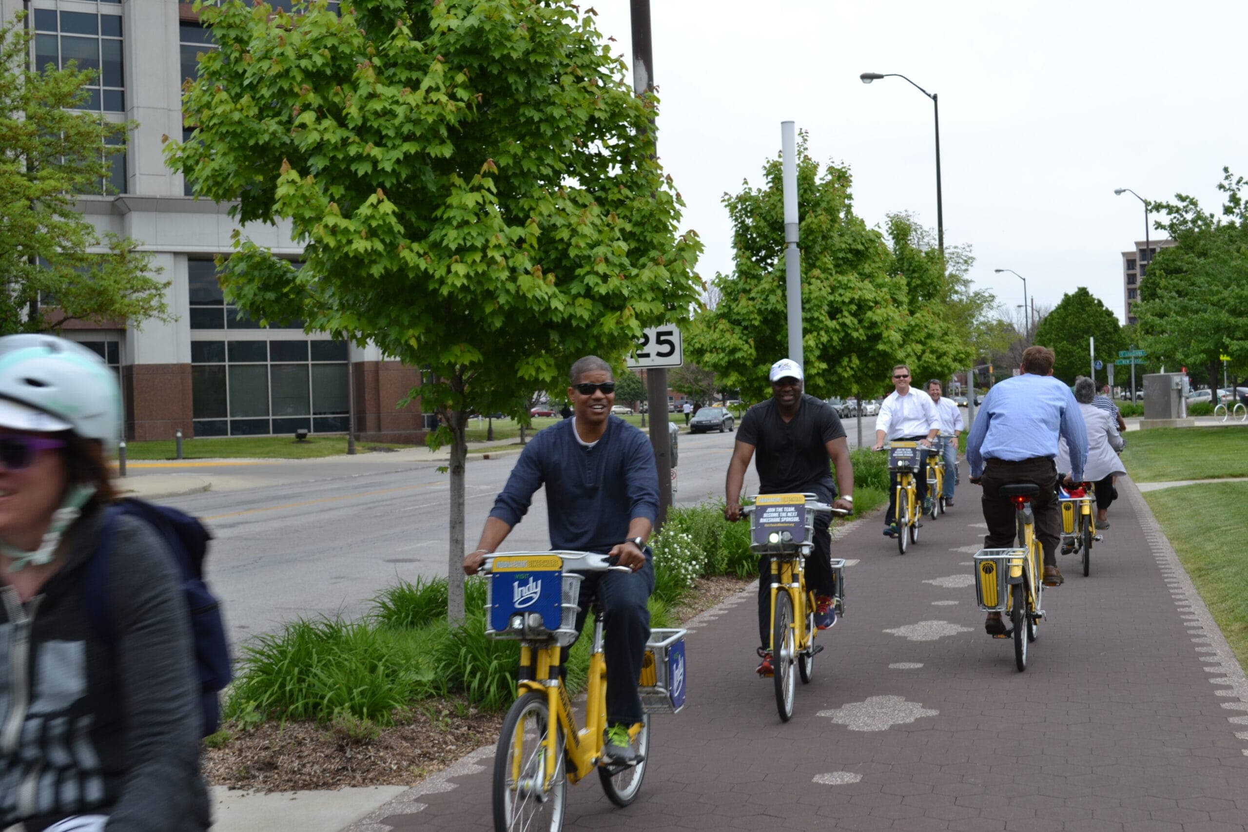 T4A Indy bike ride 2015 A group of black men ride bikes down a tree-lined path next to a 25 mph street