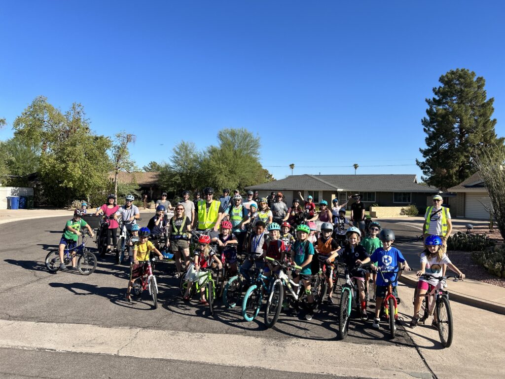 A group photo of dozens of participants of the Broadmor Bike Bus standing with their bikes near the end of a street.