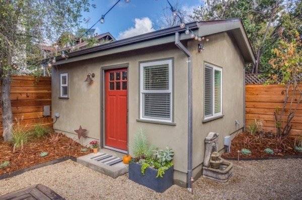a modest stuccoed ADU with a red door in the backyard of a home