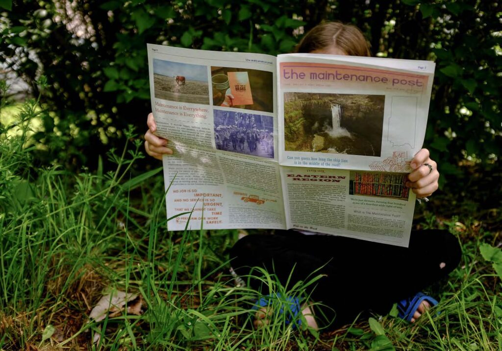 Image of person sitting on the grass and holding up a newspaper.