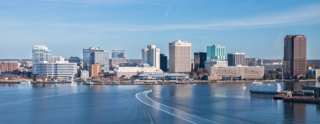 Norfolk, VA skyline shot from the water with a boat water trail and a blue sky