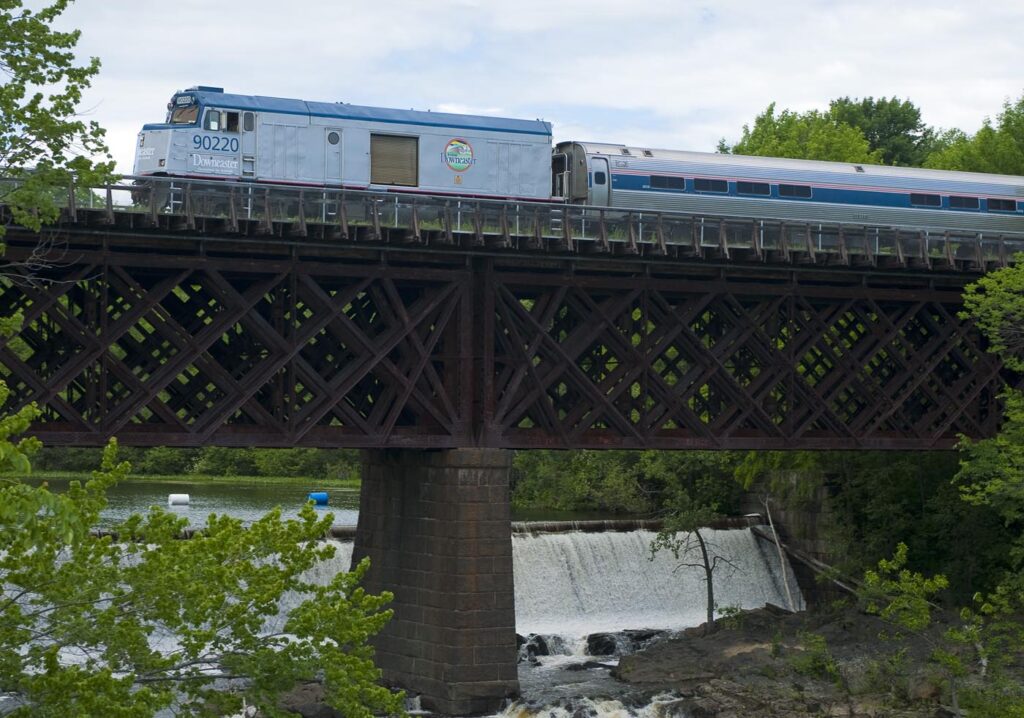 An amtrak train going over a bridge that is passing over small waterfalls and green foliage