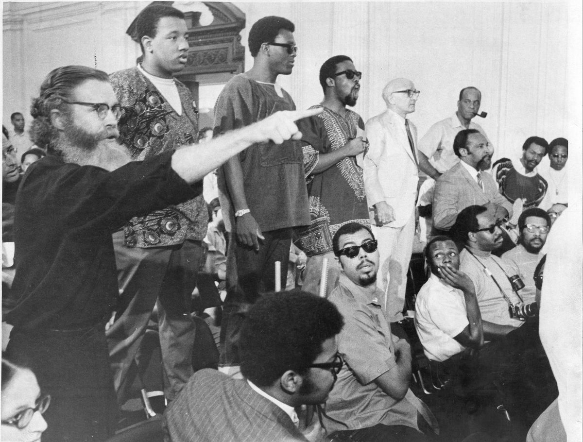 A group of Black men are flanked by two white men, all animatedly participating in a discussion