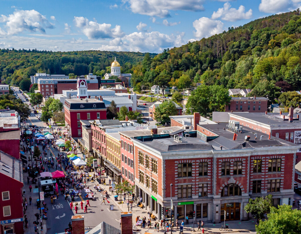 People, vendor tents, and activity on an open street in downtown Montpelier, Vermont.