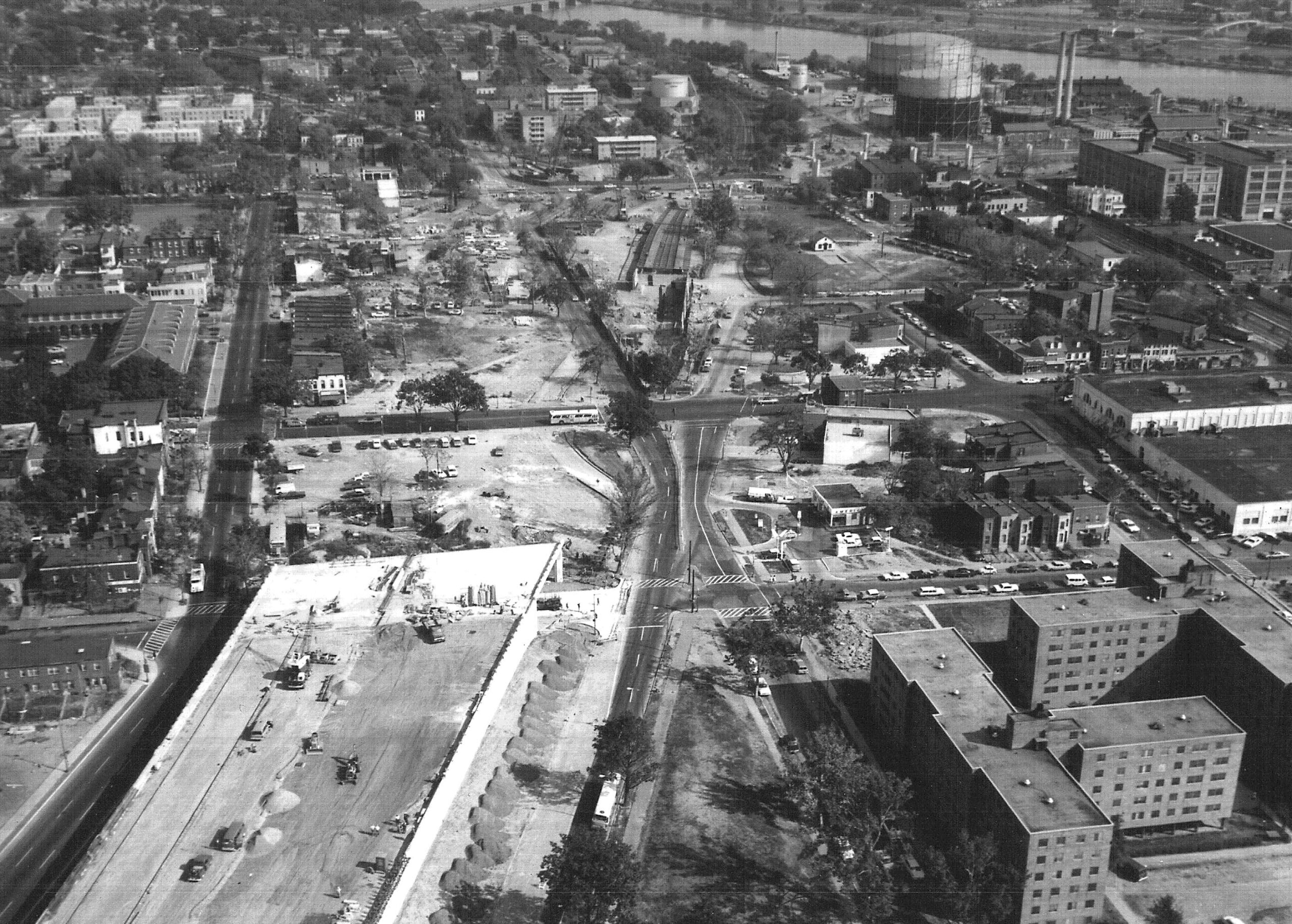 The stump of I-395/695, in the midst of construction, rises out of the lower lefthand side of the frame, facing a cleared path in an otherwise dense city. Black and white photograph 