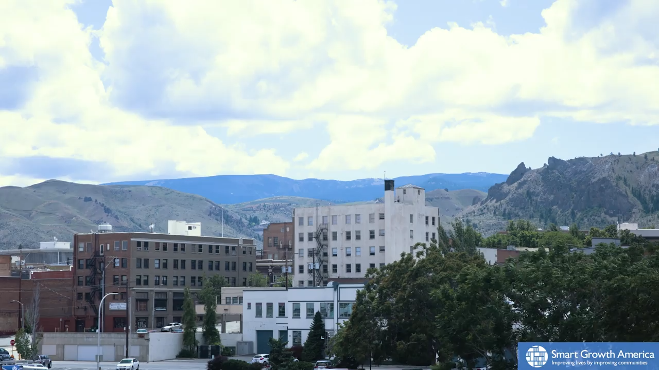 Image of the Wenatchee, WA skyline, featuring a row of brick office buildings with mountains and clouds rising in the background