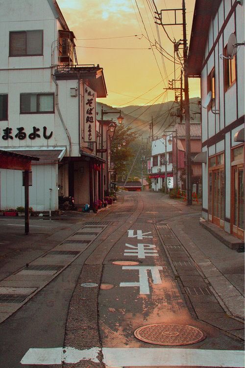 A Japanese street with a yellow sky in the background showing one car lane and a neighboring sidewalk.