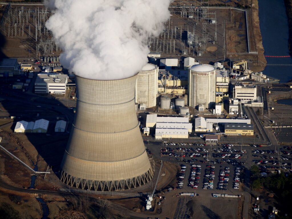 An aerial view of a nuclear cooling tower with steam coming out and surrounding facilities