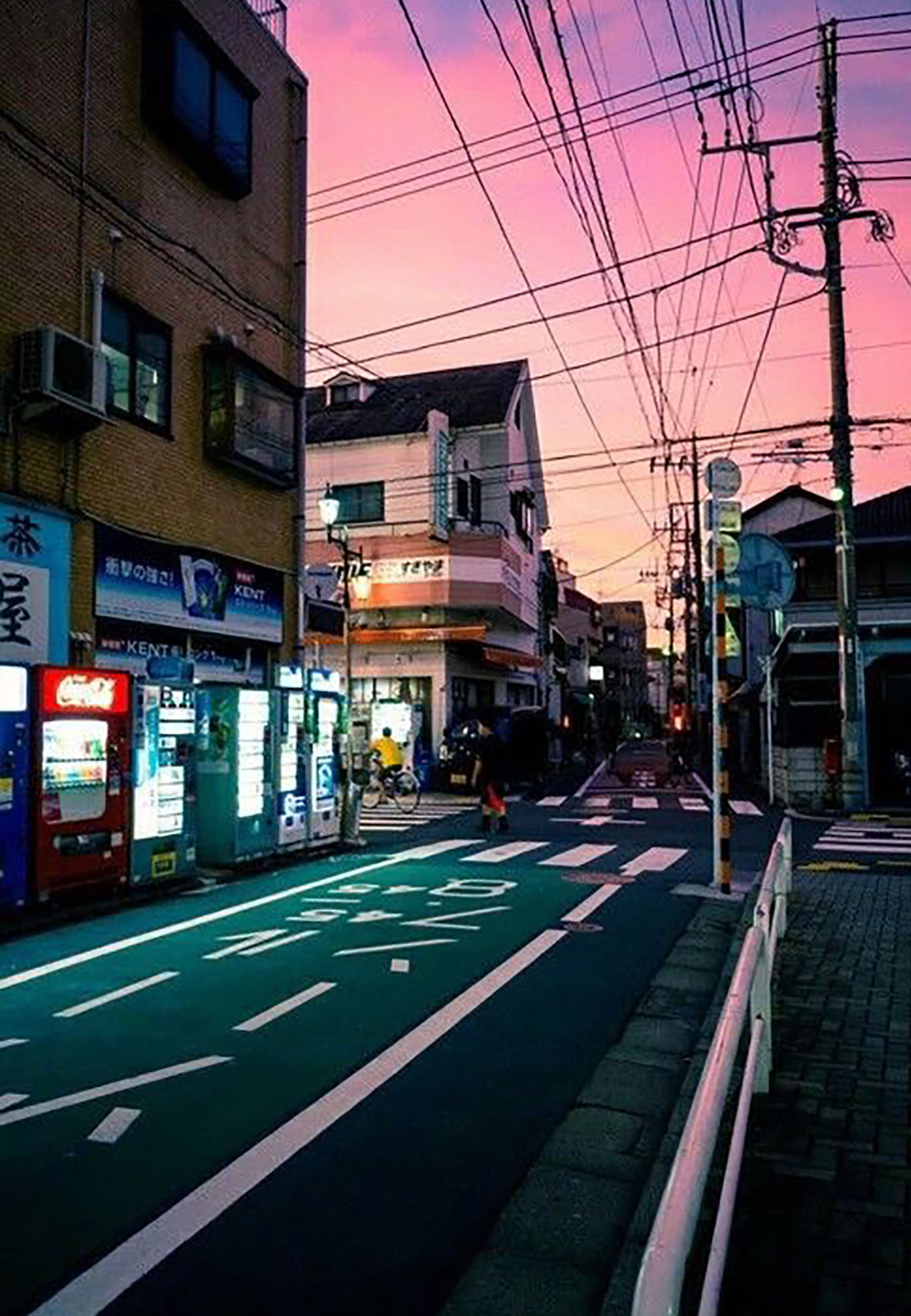 A Japanese street with a pink sky in the background showing one car lane, a bike lane, and sidewalk.