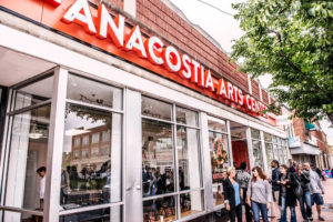A close-up photograph of the entrance of the Anacostia Arts Center, with people walking in and out