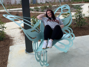 A young woman in a Harvard t-shirt lounges in a butterfly bench inside the new park, demonstrating that this is a fun place for youth to gather and rest.