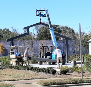 A crane places a barn's facade inside the site of Atmore's new park, while two men carry a large metal beam into position