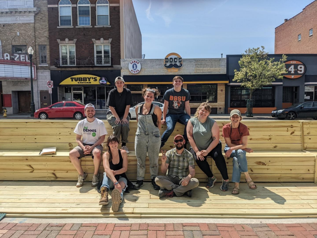 With construction of a parklet complete, a group of young people smiles triumphantly from atop the new space