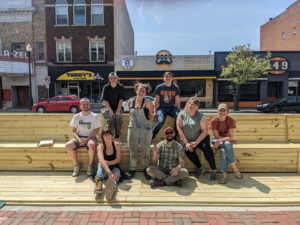 With construction of a parklet complete, a group of young people smiles triumphantly from atop the new space