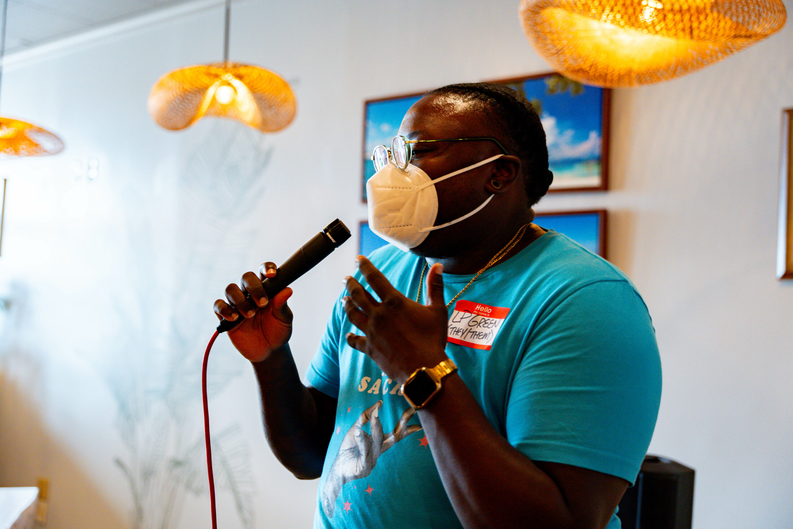 A person wearing a blue shirt and Covid-19 mask speaks into a microphone