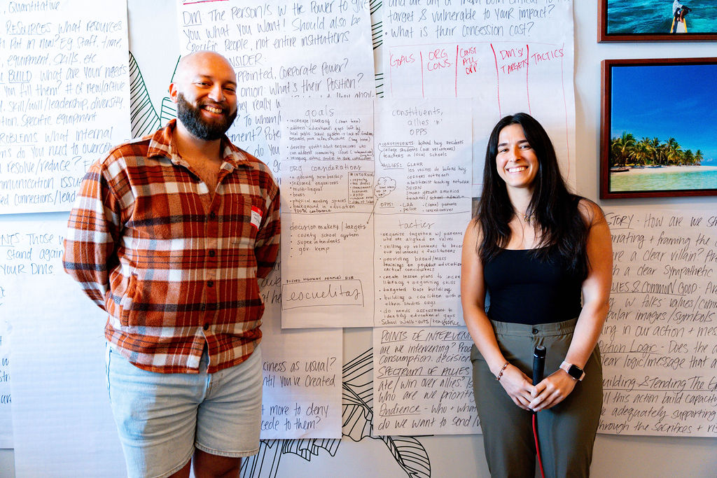 Two individuals standing against a wall with charts behind them.