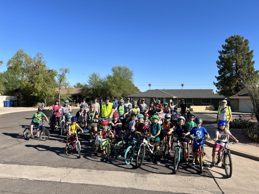 A group photo of dozens of participants of the Broadmor Bike Bus standing with their bikes near the end of a street. 