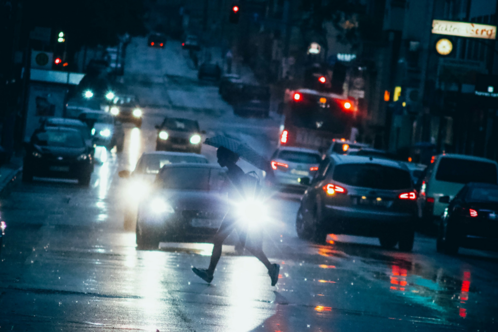 A pedestrian runs across the street as cars with bright headlights near their path