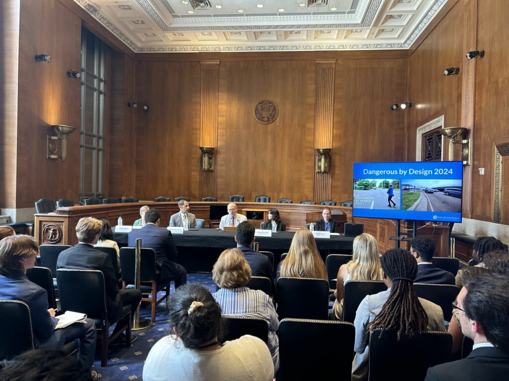A panel sits before congressional staffers inside the US Capitol. A presentation on the right shows the words "Dangerous by Design"