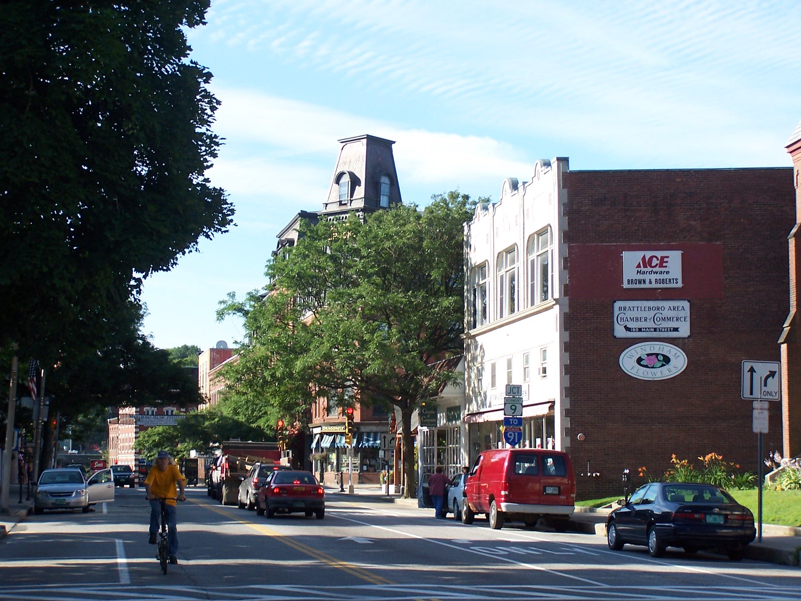 A cyclist travels down Brattleboro's tree-lined main street, near businesses.