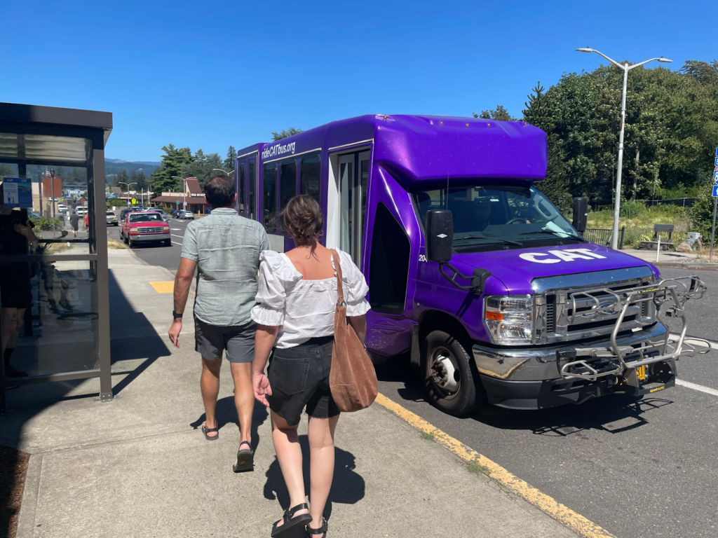 A purple bus picks up passengers in a rural area