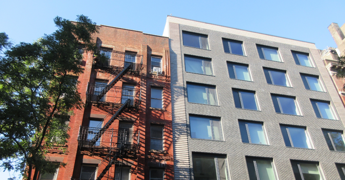 A modern gray apartment building rises beside a brown brick apartment building