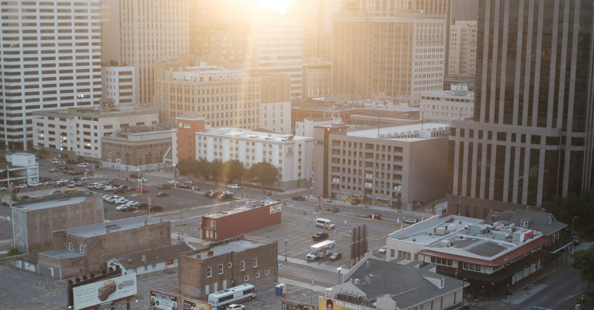 The sun sets over a large, almost entirely empty parking lot in an urban downtown