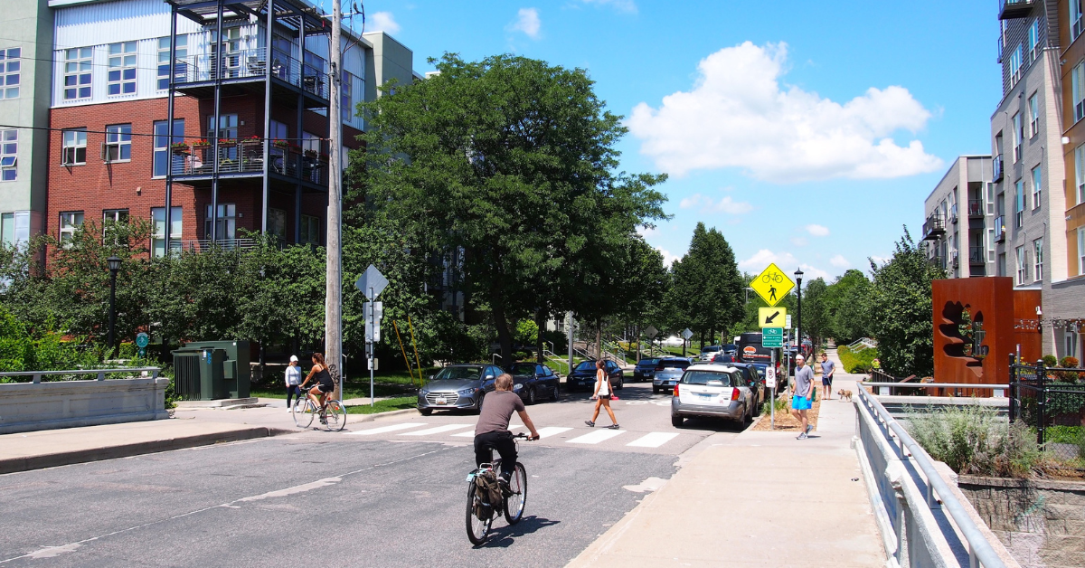 A cyclist travels down a road lined by parked cars