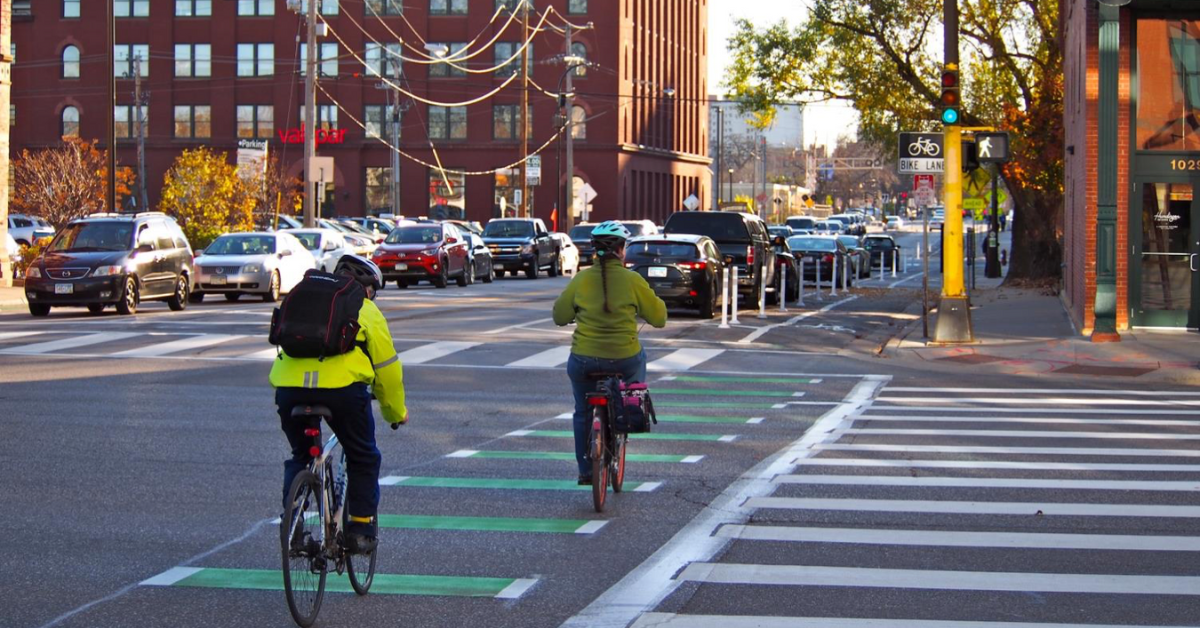 Two cyclists travel down a painted bike lane next to a signalized crosswalk in Minneapolis