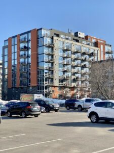 A parking lot with many empty spaces sits beside an apartment building