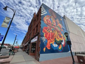 A colorful photo of a building with a mural of a woman in a bright pink and orange dress in Pittsfield, MA.