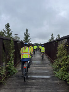 Cyclists in yellow vests travel down a wooden bridge on the American Tobacco Trail