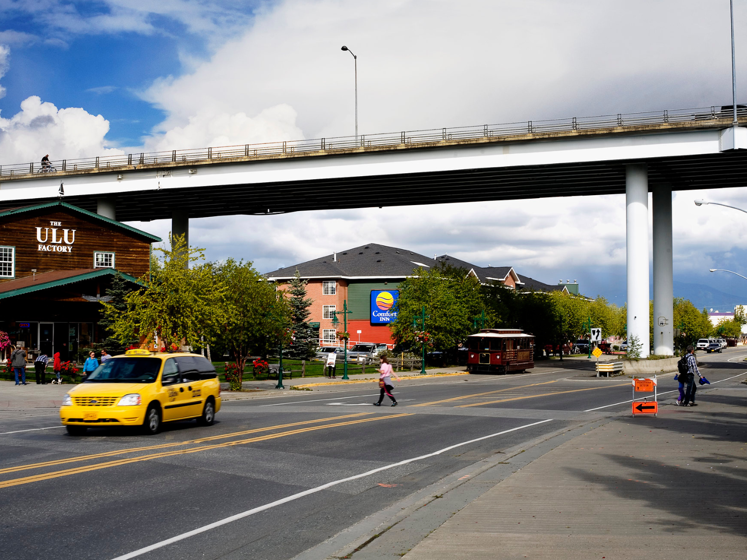 A pedestrian crosses the street while a cyclist uses an overpass on a wide open road in Anchorage, Alaska