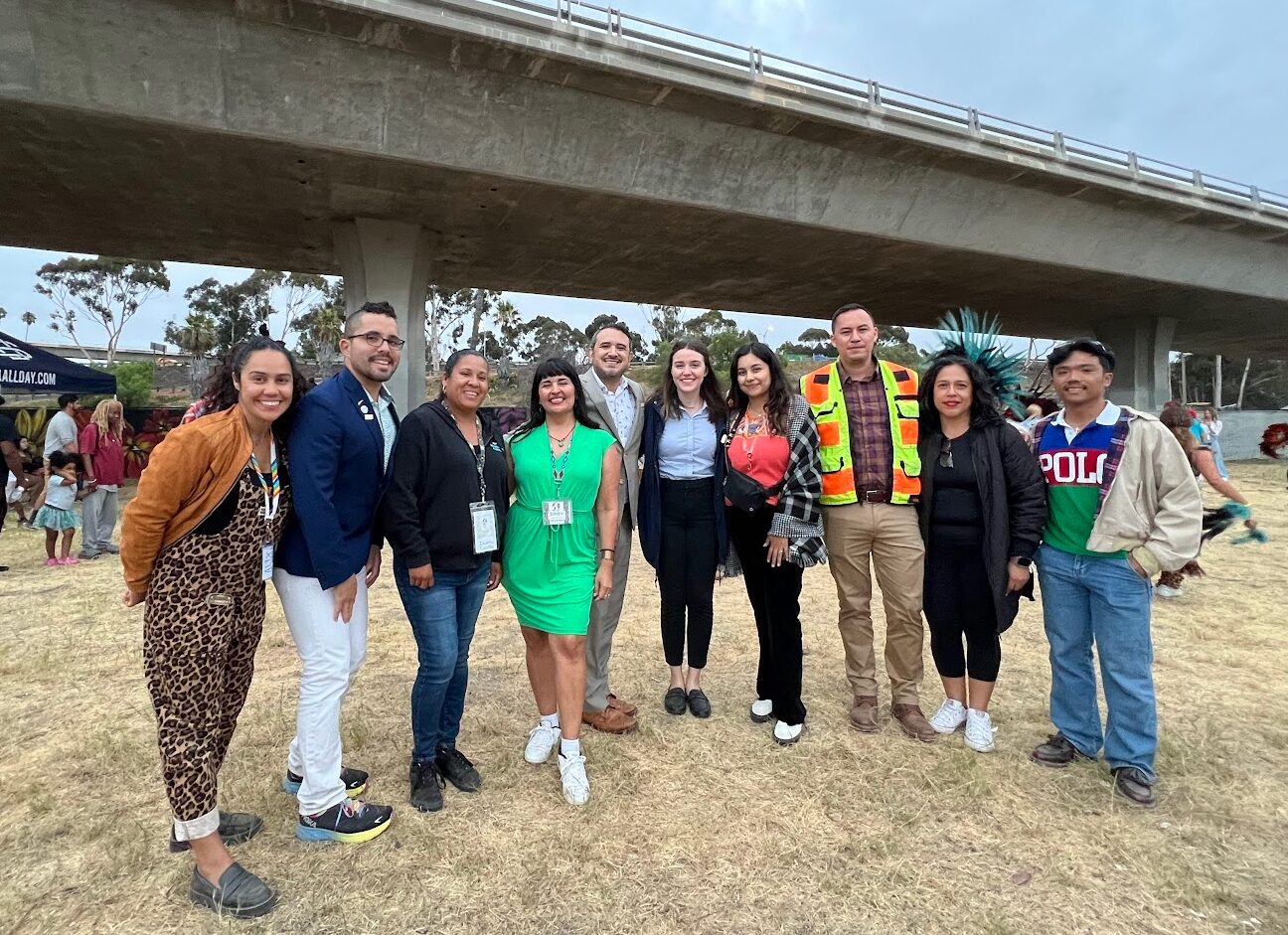 A group of people smile at the camera from beneath a highway overpass