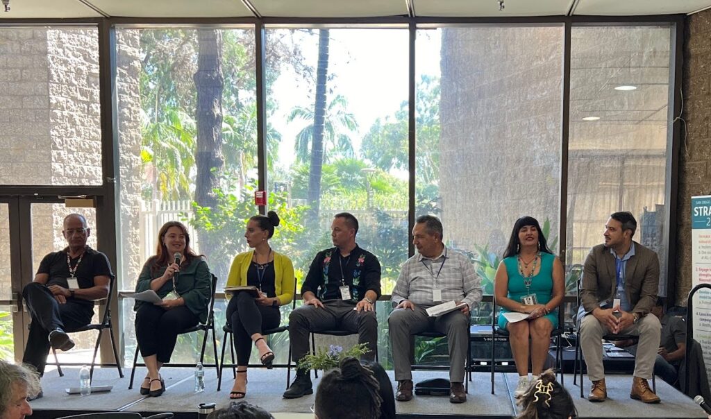 A row of panelists on a sunlit stage