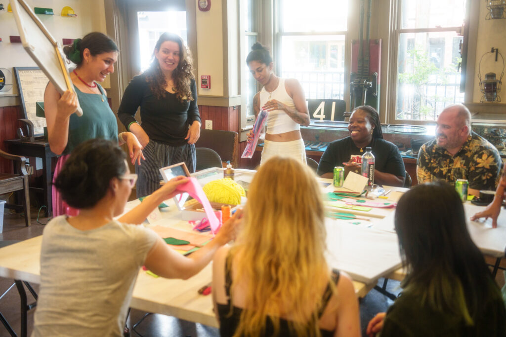 People of all ages and backgrounds gather around a table set with different types of art supplies.